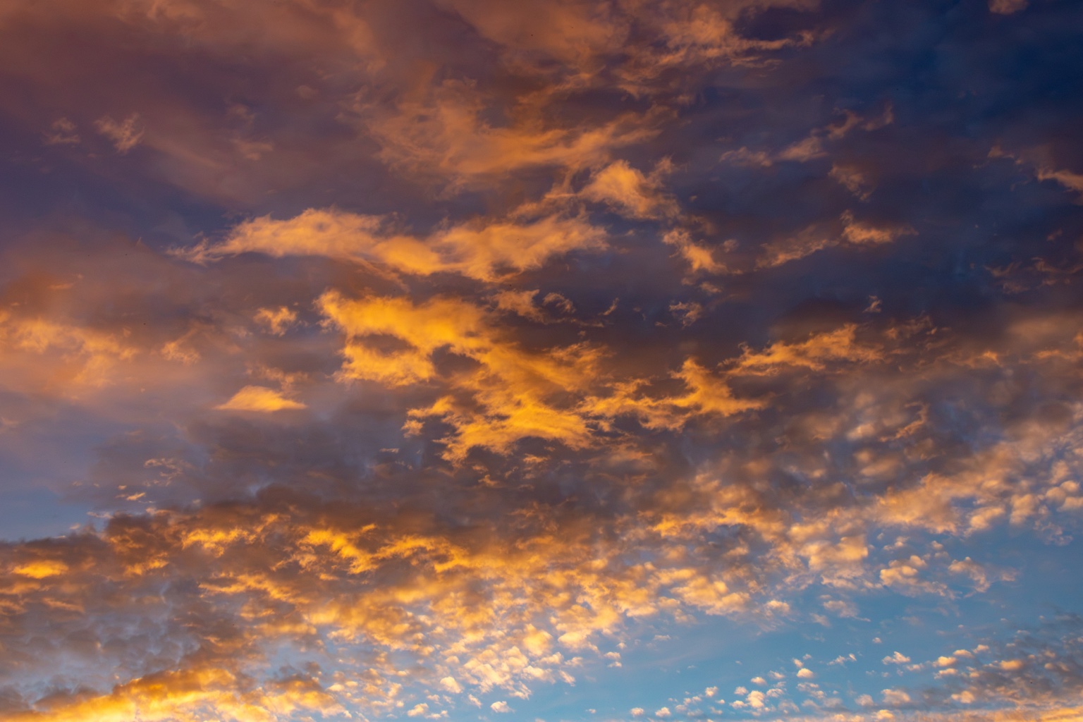 Weite Wolkenlandschaft mit orangegoldenen Rändern, dunkelblauen Wolken und hellblauem Himmel