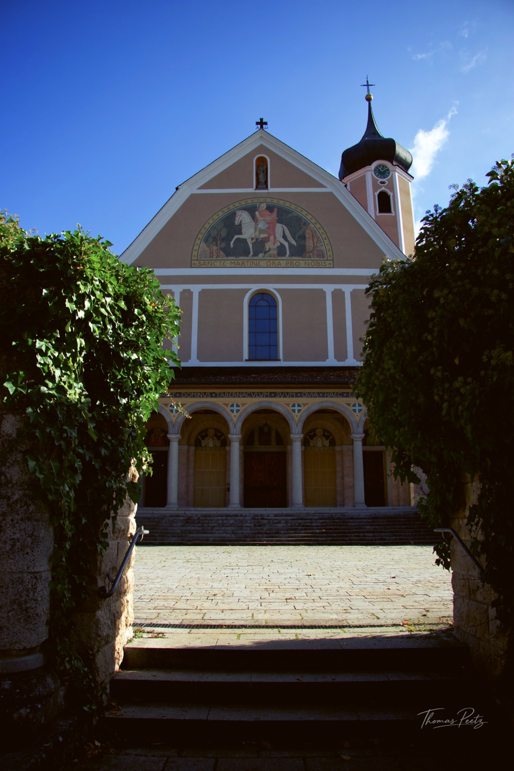 Blick über Stufen und zwischen begrünten Mauern zur Fassade der Klosterkirche in Beuron