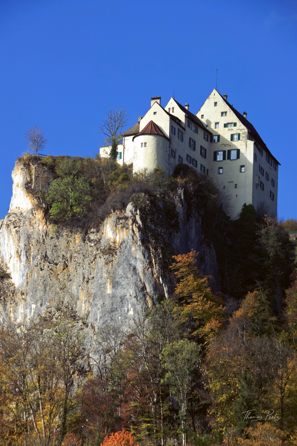 Naher Blick auf das helle Schloss und seinen steilen Felsuntergrund vor blauem Himmel