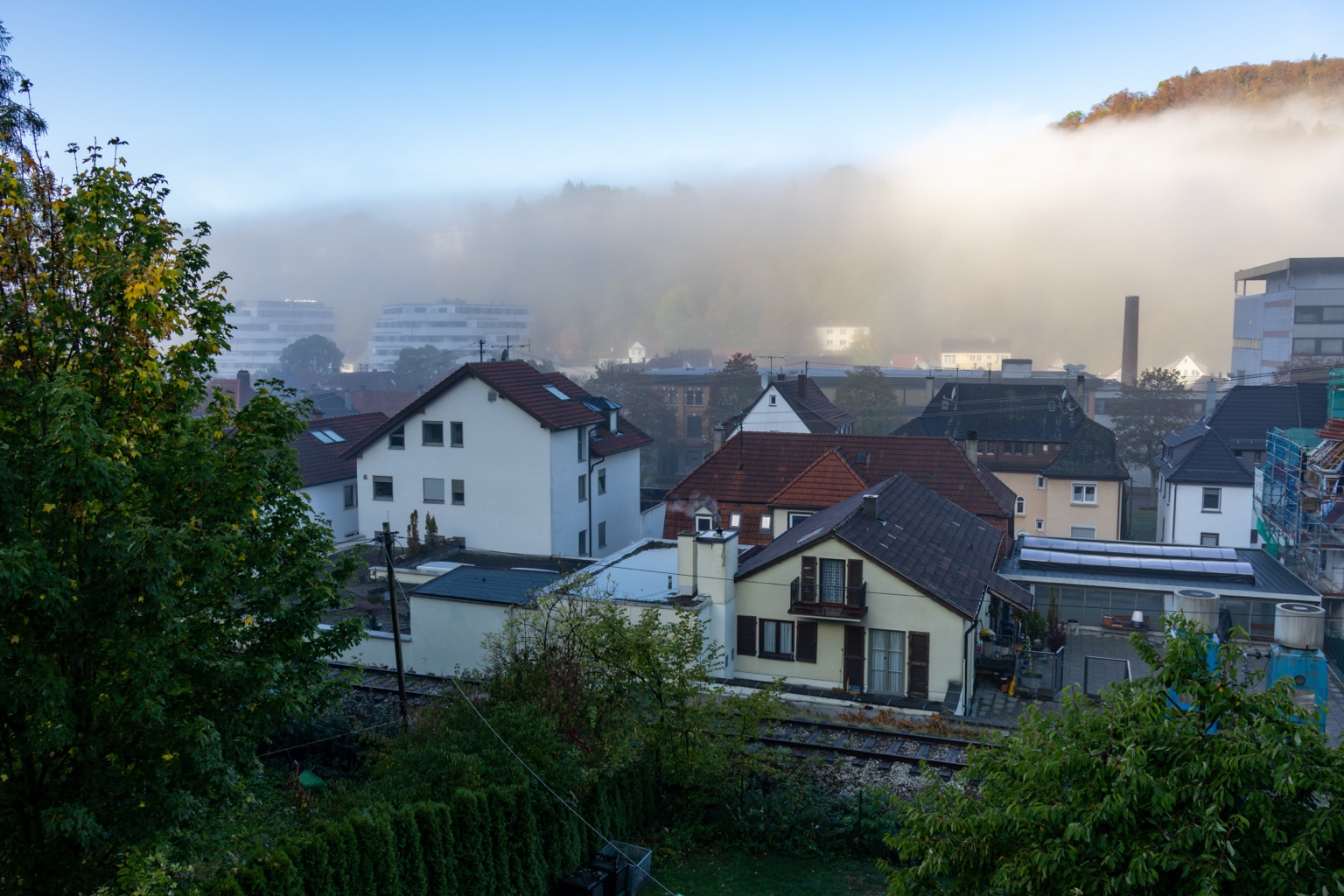 Sonnenlicht hellt den Nebel hinter den Dächern von Ebingen auf, am oberen Rand erscheint ein herbstlicher Waldhang