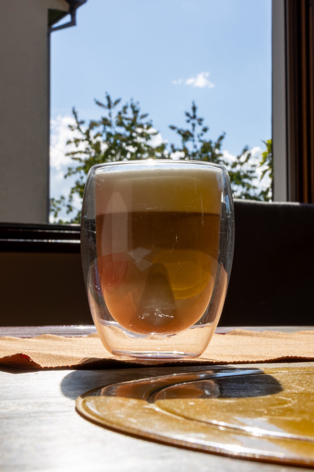 Ein Glas am Fenster im Sonnenlicht mit warmen Farbtönen und Schatten auf dem Tisch