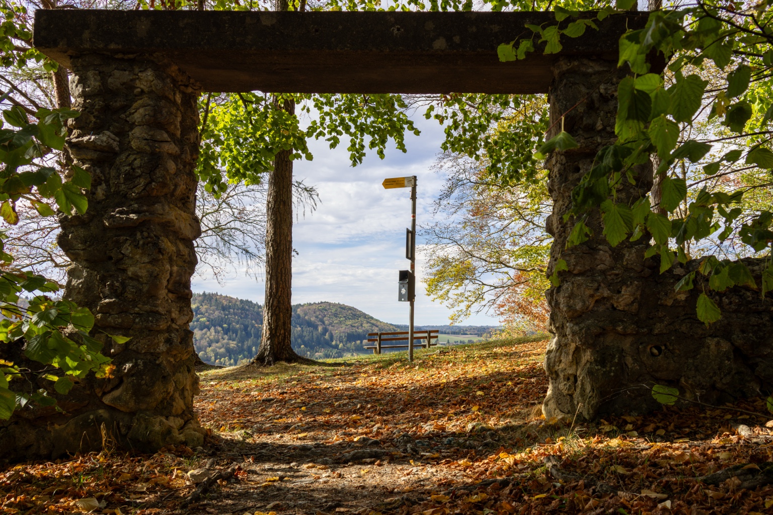 Steinernes Tor mit Blick auf herbstliches Laub, einen Baum und die Landschaft