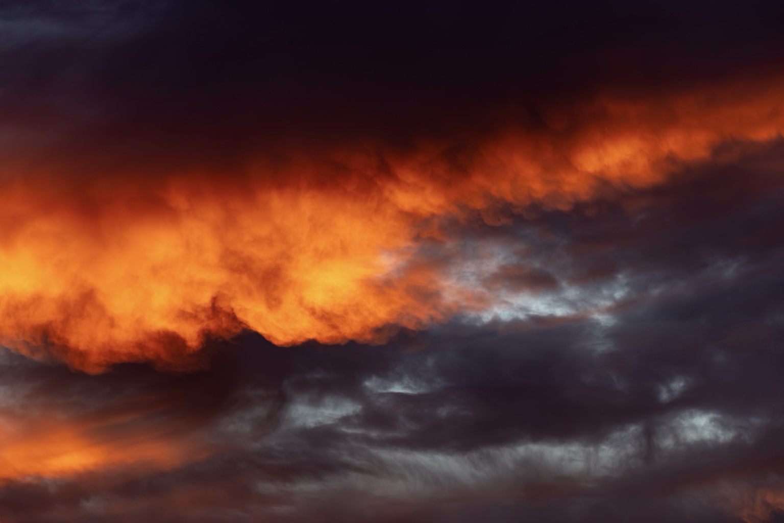 Naher Ausschnitt einer intensiv orange leuchtenden Wolkenkante vor graublauen Wolken