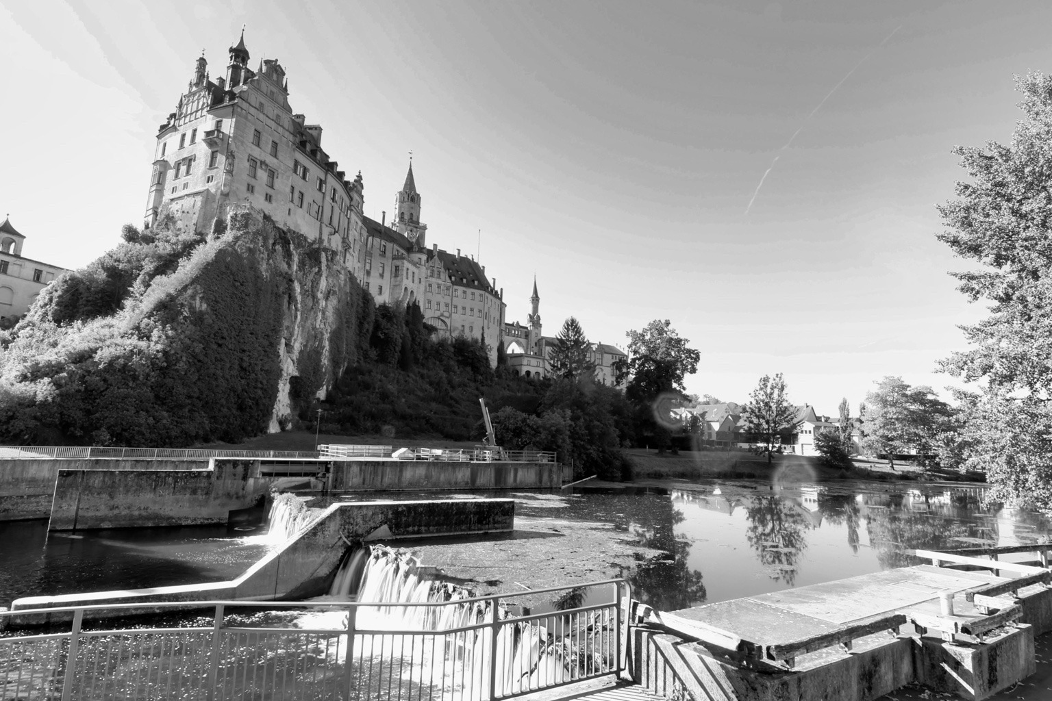 Schwarzweißaufnahme von Schloss Sigmaringen über der Donau mit Uferanlagen und Spiegelungen