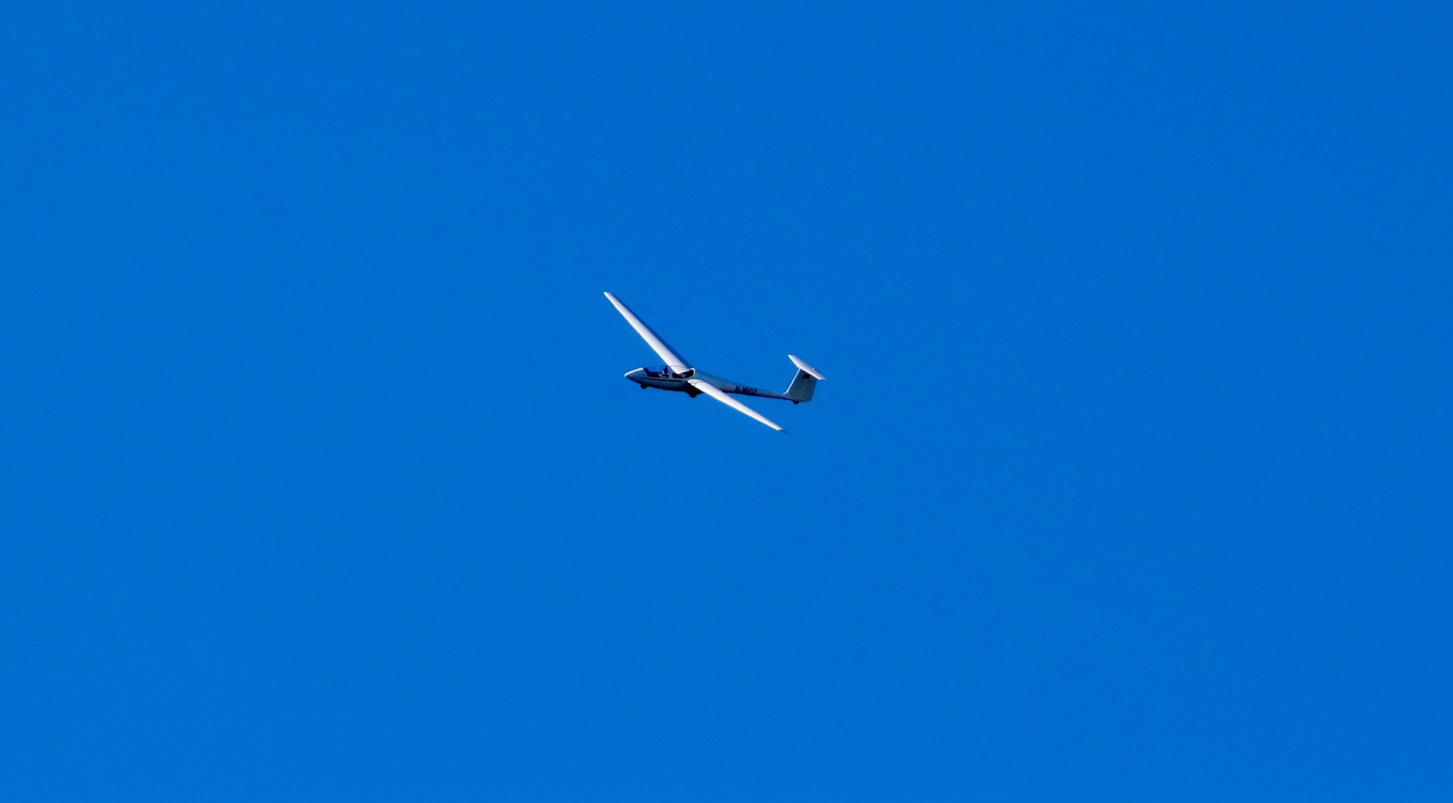 Weißes Segelflugzeug mit langen Tragflächen schräg am tiefblauen Himmel